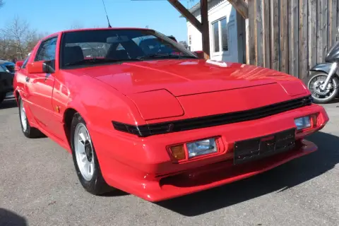 Czerwony Mitsubishi Starion z lat 80. błyszczy w słońcu. Klasyk sportowy z wysuwanymi światłami.