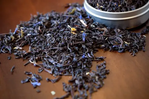 Garść liści aromatycznej herbaty earl grey, z niebieskimi płatkami chabru, rozsypana na drewnianym blacie.