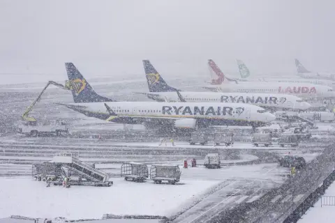 Samoloty Ryanair i Lauda stoją na lotnisku podczas zamieci. Sprawdź, jak sprawdzić powód opóźnienia lotu w takich warunkach.