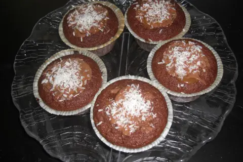 Fem kladdkakemuffins med kola och kokosflingor på ett glasfat.