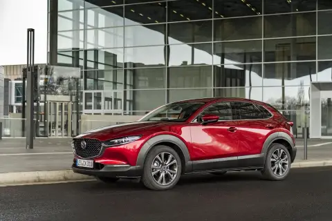 Czerwona Mazda CX-30 lśni przed nowoczesnym budynkiem z przeszkloną fasadą.