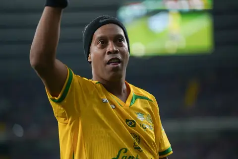Ronaldinho w żółtej koszulce z zielonymi akcentami, podnosi rękę.