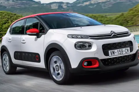 Biały Citroen C3 2025 z czerwonym dachem i lusterkami jedzie po drodze, otoczony zielonymi wzgórzami.