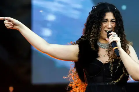 Una delle tanti artisti primo maggio, canta con passione sul palco, indicando il pubblico con un gesto energico.