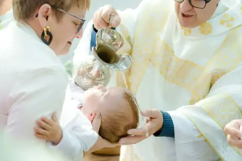 Chrzest dziecka. Kapłan polewa główkę niemowlęcia wodą święconą. Warto wiedzieć, ile kosztuje chrzest, by odpowiednio się przygotować.