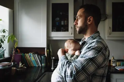 Tata po francusku, czyli "papa", czule tuli swoje śpiące dziecko w kuchni.