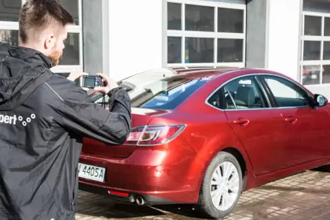 Mężczyzna robi zdjęcie czerwonego samochodu, który jest na sprzedaż bezpośrednio od właściciela.