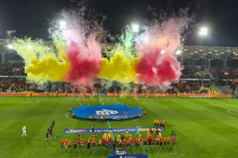 Oprawa meczu Korona Kielce – Jagiellonia Białystok. Piłkarze wychodzą na murawę w otoczeniu gęstego dymu w barwach żółto-czerwonych.