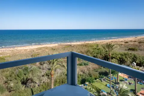 Vista desde balcón de hotel, mar azul, playa con gente y vegetación. Opiniones de hotel Playas de Guardamar positivas.