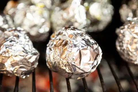Ziemniaki z grilla zawinięte w folię aluminiową, piekące się nad żarem.