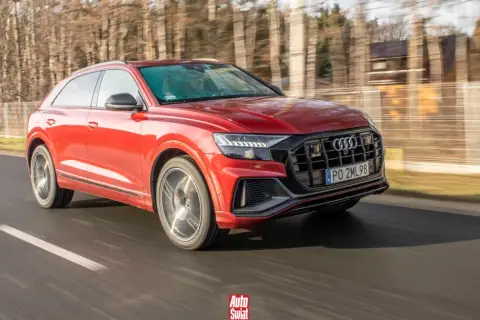 Czerwone Audi SQ8 pędzi po drodze, otoczone rozmazanym lasem.
