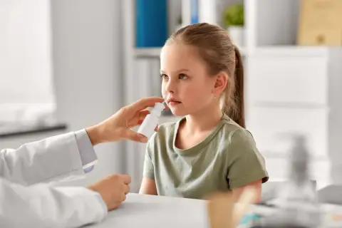 Niña recibe spray nasal para aliviar síntomas de rinitis alérgica. El doctor investiga las causas.