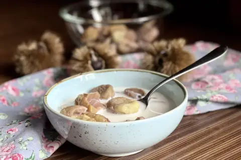 Una ciotola di castagne al latte, un dolce autunnale cremoso e confortante, con ricci di castagne sullo sfondo.