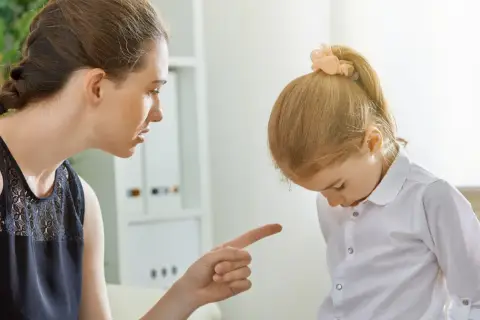 Matka karci córkę za złe zachowanie, wskazując palcem. Dziewczynka spuszcza wzrok, zawstydzona.