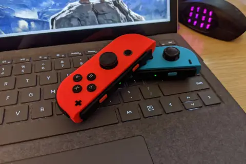 Czerwony i niebieski Joy-Con na klawiaturze laptopa, gotowe do gry. Dowiedz się, jak podłączyć Nintendo do komputera.