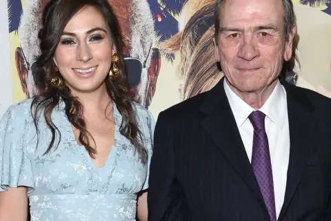 Tommy Lee Jones z żoną, uśmiechnięci na tle plakatu filmowego.