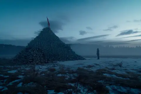 Un uomo solitario osserva un'enorme piramide di teschi in un paesaggio innevato. Un'immagine che evoca le recensioni de "The Revenant".