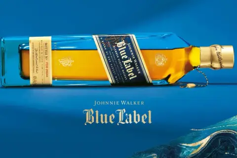 Elegancka butelka Johnnie Walker Blue Label leży na niebieskim tle. Złoty płyn i niebieskie szkło tworzą luksusowy kontrast.