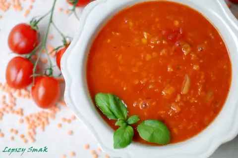 Zupa pomidorowa z soczewicą, ozdobiona bazylią. Obok gałązka pomidorków i rozsypana soczewica. Idealna na chłodne dni, smakuje jak domowe pesto pomidorowe.