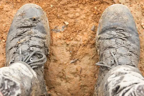 Mud-caked boots, laces frayed, look like they're falling apart after a tough hike.
