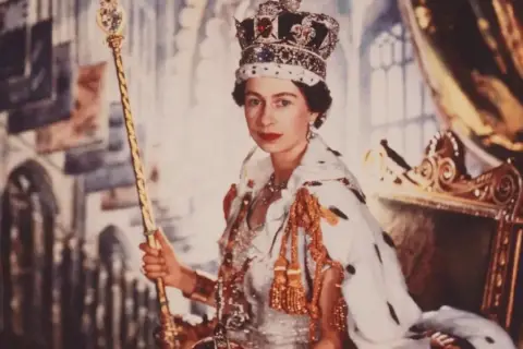 Elizabeth II av Storbritannien, krönt och med spira, sitter på tronen i sin kungliga dräkt.