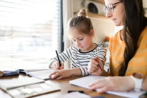 Dziewczynka z mamą uczą się w domu. Jak zacząć edukację domową? Skupienie na nauce i wsparcie rodziców.