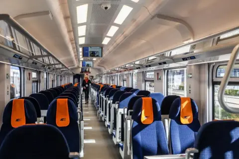 Wnętrze nowoczesnego wagonu PKP Intercity. Siedzenia w kolorze granatowym z pomarańczowymi zagłówkami. Ile wagonów ma pociąg IC? To zależy od trasy i typu składu.