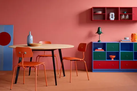 Ein Essbereich mit orangefarbenen Stühlen und einem Holztisch vor einer korallenroten Wand. Die Wandfarbe erinnert daran, wie man dunkelrot mischt.
