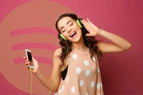 Dziewczyna z słuchawkami na uszach i telefonem w dłoni, ciesząca się muzyką. Idealna okazja, by sprawdzić Spotify Premium za 0,99!