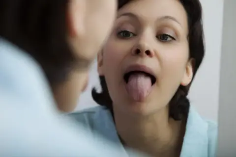 Donna si guarda allo specchio, mostrando la lingua. La saliva aiuta a digerire e a mantenere la bocca sana.