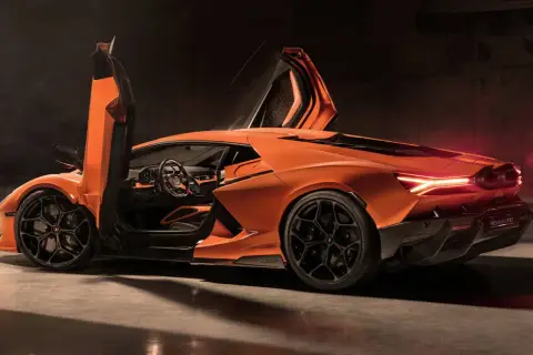 Pomarańczowy Lamborghini Revuelto z otwartymi drzwiami typu nożycowego, z widocznym wnętrzem i sportowymi felgami.