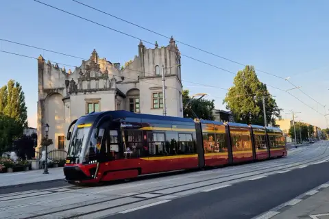Nowoczesny tramwaj pabianice z czerwono-żółtymi pasami jedzie w stronę zabytkowego budynku.
