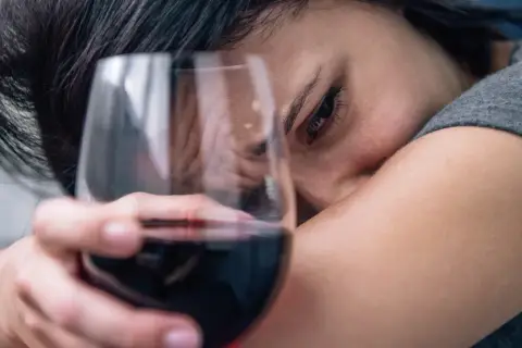 Smutna kobieta z kieliszkiem wina, symbolizująca 6 objawów uzależnienia od alkoholu.