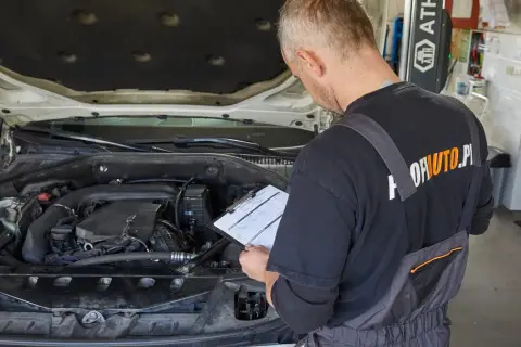Mechanik sprawdza dokumentację przy otwartej masce samochodu. Czy wymiana oleju poza ASO a gwarancja to dobry pomysł?