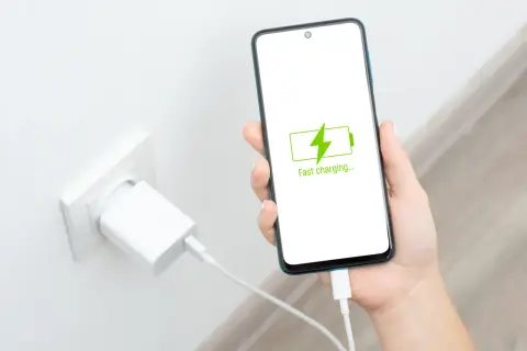 Dłoń trzyma smartfon z ikoną szybkiego ładowania. Obok w gniazdku wtyczka ładowarki. Oszczędzanie baterii nigdy nie było tak proste.