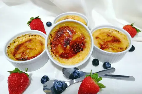 Cuatro cremosos creme brulee con una capa caramelizada, adornados con fresas y arándanos frescos.