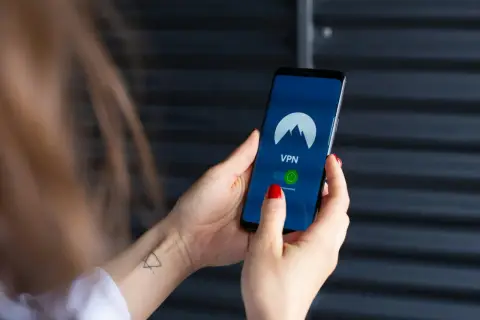 Dłoń trzyma smartfon z włączoną aplikacją VPN, gotową do zabezpieczenia połączenia, jak w najnowszych wersjach android 15.