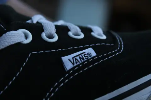 Zbliżenie na czarną tkaninę buta Vans z białymi sznurówkami i charakterystyczną metką.