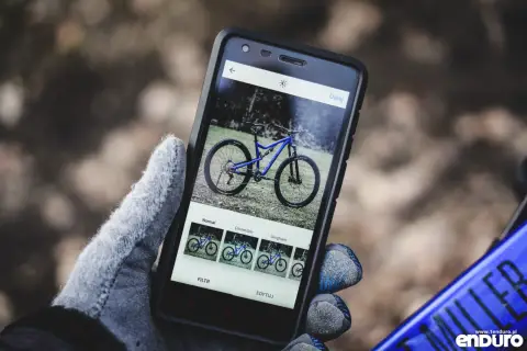 Rękawiczka trzyma smartfon z niebieskim rowerem na ekranie. Aplikacja oferuje filtry, jak w mapach rowerowych.