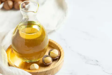 Aceite de macadamia para que sirve: un frasco de vidrio con aceite dorado y nueces de macadamia en un plato de madera.