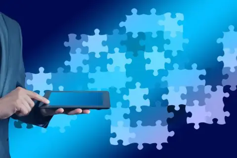 Biznesmen w garniturze trzyma tablet, a za nim układanka z puzzli symbolizuje wiedzę i rozwiązanie.