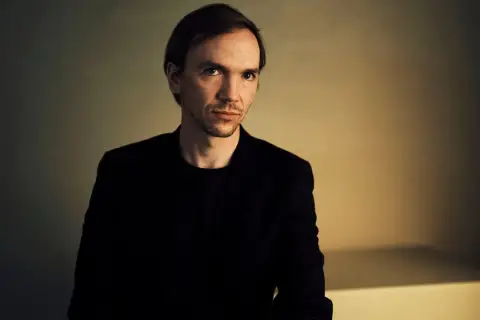 Portret Jana Komasy, reżysera znanych filmów. Jego spojrzenie sugeruje głębię i skupienie, jak w jego kinowych dziełach.