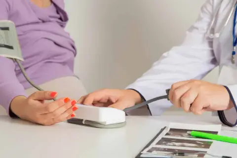 Lekarz mierzy ciśnienie ciężarnej pacjentce, monitorując jej stan pod kątem ryzyka **preeklampsji**.