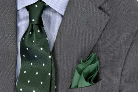 Elegancki zestaw: niebieska koszula, zielony krawat w groszki i szara marynarka. Idealna odpowiedź na pytanie: jaki krawat do niebieskiej koszuli.