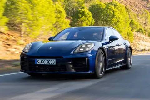 Niebieski Porsche Panamera 2024 pędzi po krętej drodze wśród zielonych wzgórz.