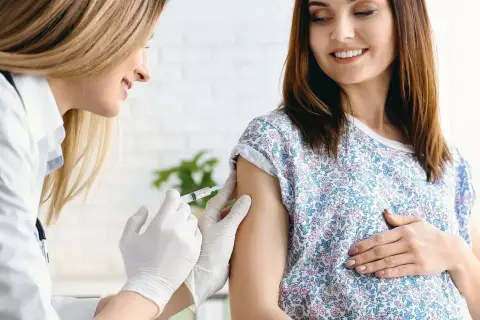 Ärztin verabreicht schwangerer Frau Impfung. Boostrix Polio schützt Mutter und Kind.