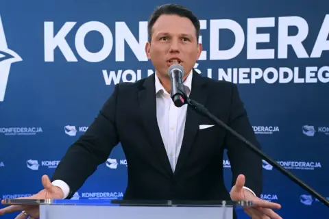 Mężczyzna w garniturze przemawia do mikrofonu na tle baneru Konfederacji. Dyskutuje, dlaczego KO chce odebrać dotacje partii opozycyjnej poprzez nowelizację kodeksu wyborczego.