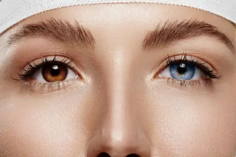 Oczy z **heterochromią centralną**: jedno brązowe, drugie niebieskie. Wokół nich delikatna skóra i podkreślone rzęsy.