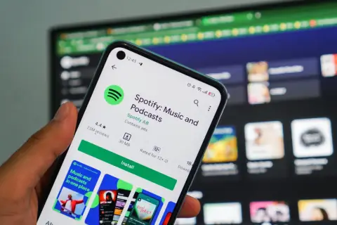 Dłoń trzyma smartfon z ekranem sklepu Google Play, gdzie widoczna jest strona aplikacji Spotify. To świetna okazja, by skorzystać z **spotify promocja** i pobrać ulubioną muzykę i podcasty.