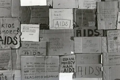 Ludzie błagają o pomoc, umierają na AIDS. Kartony z napisami "SOS", "Help", "Proszę o pomoc" świadczą o desperacji i walce o życie w obliczu choroby, która w tamtych czasach była naznaczona stygmatyzacją i brakiem wsparcia, tworząc swoistą **hegemonię*...